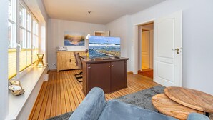 Una sala de estar acogedora con una televisión grande, piso de madera, un sofá y una pequeña mesa de madera.