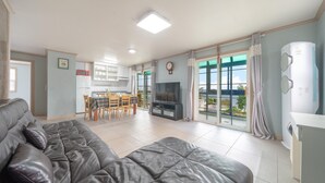 Una sala de estar moderna con un sofá de cuero, un comedor con televisor y ventanas amplias que ofrecen vistas al exterior.