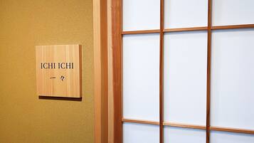 Une enseigne en bois, ornée de caractères japonais, est fixée à un mur, à côté d’une porte coulissante traditionnelle à motifs géométriques.
