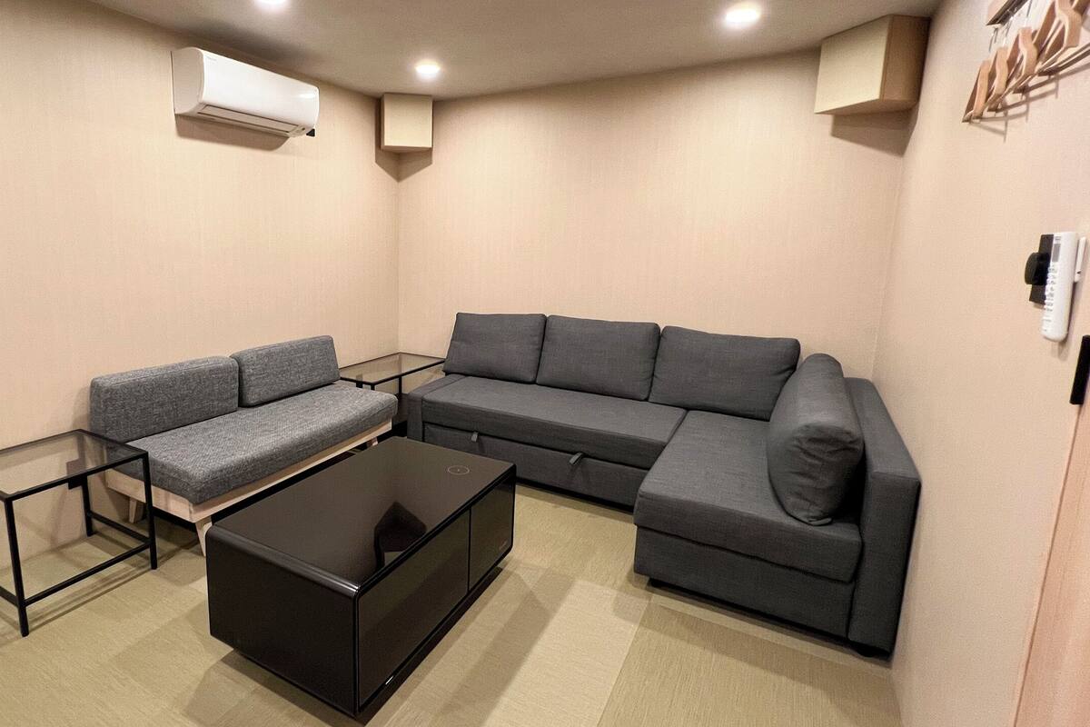 Una sala moderna con un sofá seccional gris, una mesa de centro de vidrio y un mueble de televisión negro.