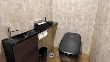 Un baño con un lavamanos negro, un inodoro y un cubo de basura.