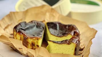 A pastry with a golden-brown top, possibly a custard or cream-based dessert, in a paper-lined container.