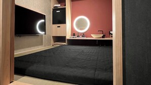Una habitación pequeña con cama, televisión, espejo y baño.