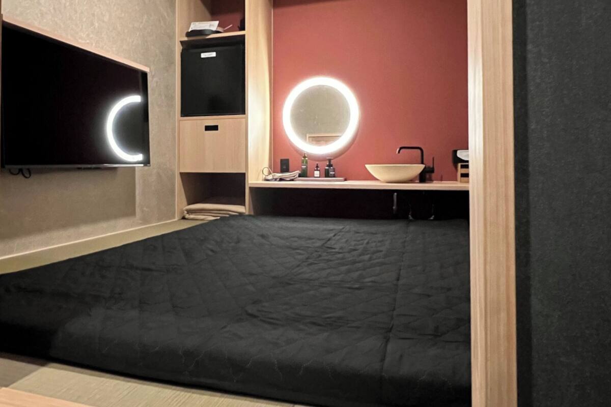 Una habitación pequeña con cama, televisión, espejo y baño.