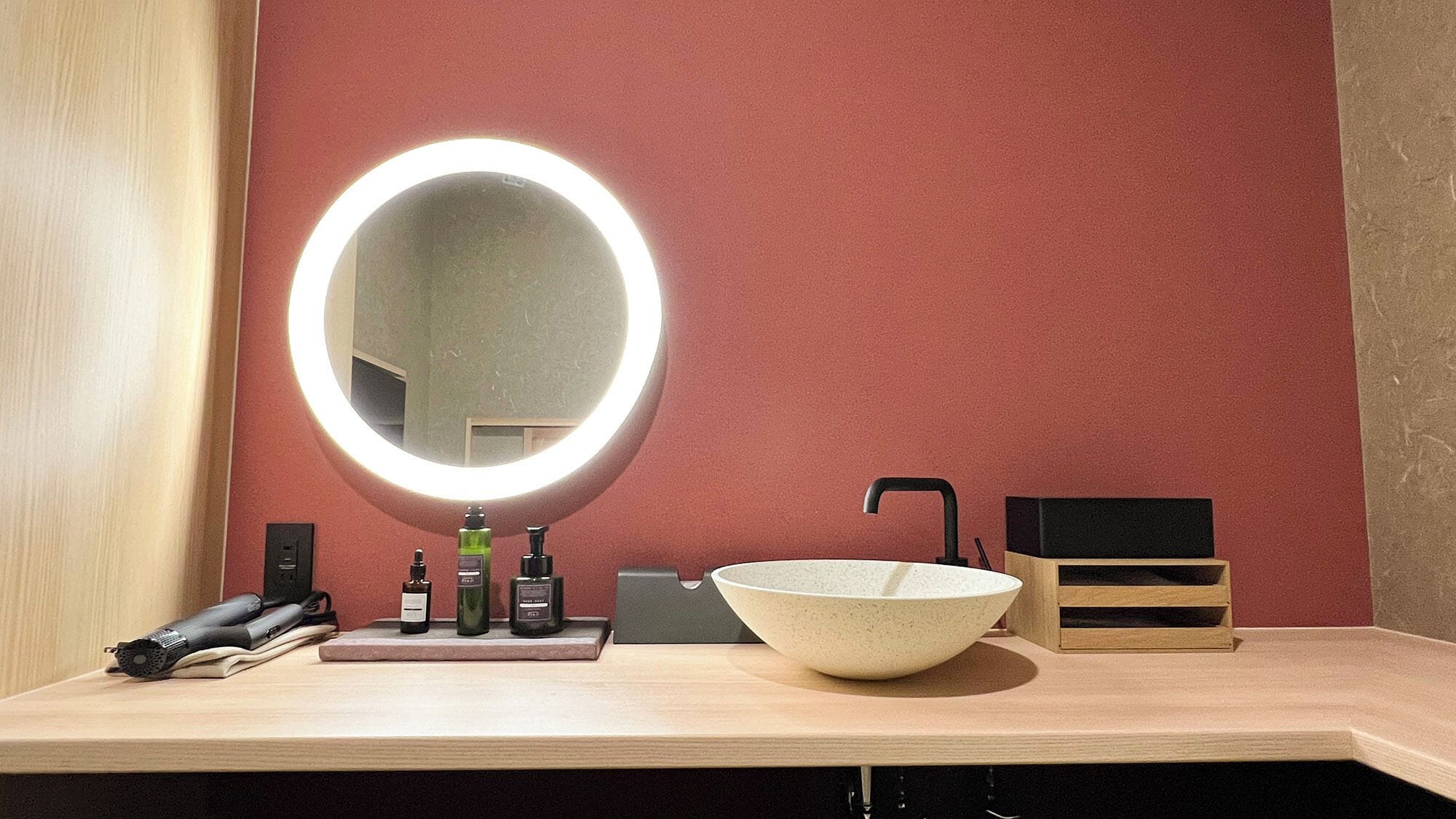 A bathroom with a round mirror, a sink, and toiletries.