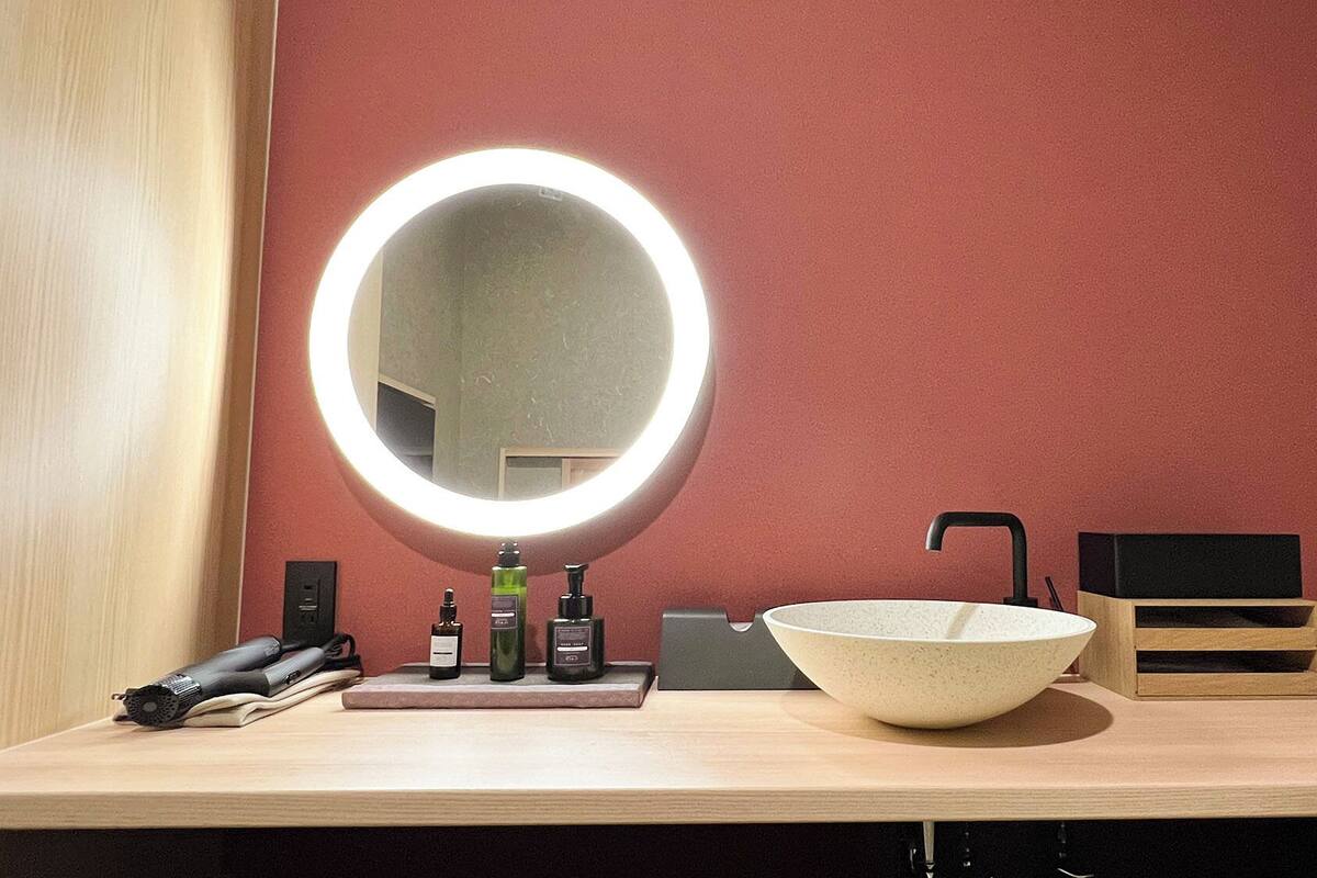 Un baño con un espejo redondo, un lavamanos y artículos de aseo.