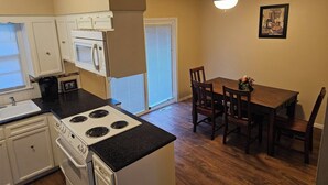 Une cuisine compacte équipée d’une cuisinière, d’un four à micro-ondes et de placards, jouxtant un coin repas avec une table et des chaises.