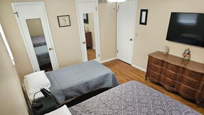 Une chambre avec deux lits, une commode, une télévision et un miroir.