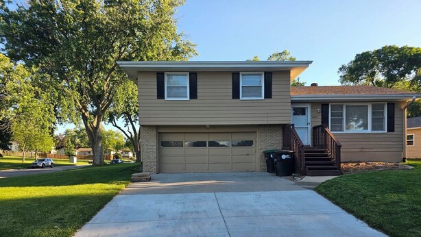 Une maison à deux étages avec un garage, un jardin devant et une allée.