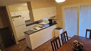 Une cuisine de taille réduite avec des meubles blancs, un plan de travail noir et une table à manger avec des chaises.