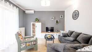 A modern living room with a grey sofa, a wooden bench, and a TV in the background. - Nice apartment in Bresca with WiFi (Bresca)