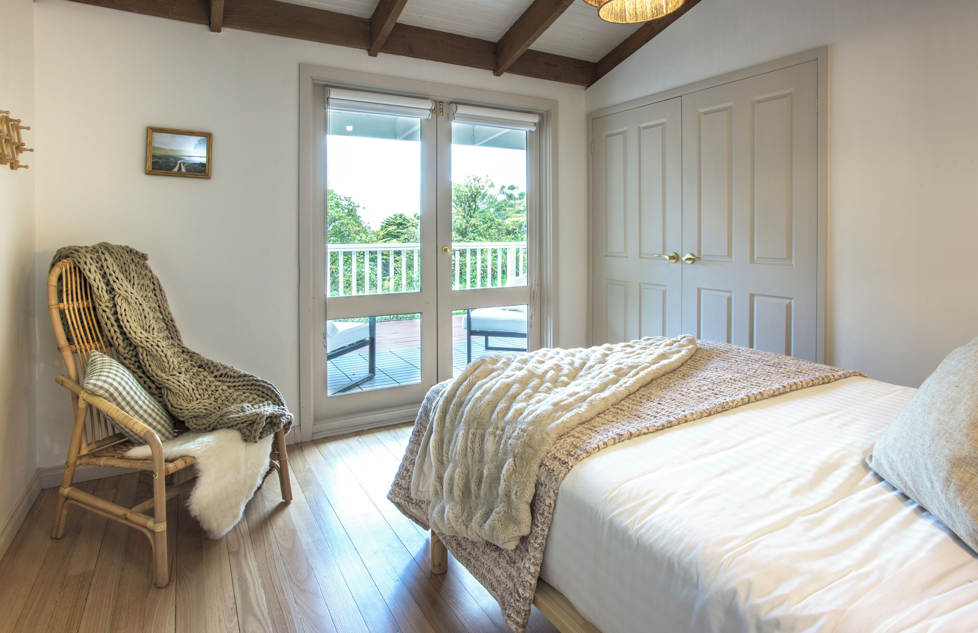 A bedroom with a bed, a chair with a blanket, a door, and a window with a view of greenery.