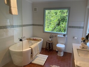 A bathroom with a bathtub, toilet, and sink, featuring a window with a view of greenery. - Woolrich House at Woolrich Estate (Olinda)