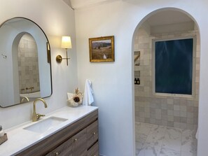 A bathroom with a large mirror, a sink with a gold faucet, a framed picture on the wall, and a shower with a blue curtain. - Woolrich House at Woolrich Estate (Olinda)