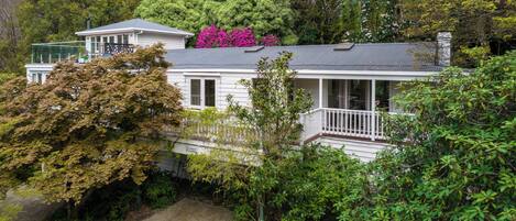 A two-story house with a covered porch, surrounded by dense greenery and trees.