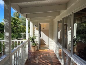 A covered porch with a wooden deck, white railings, and potted plants. - Woolrich House at Woolrich Estate (Olinda)
