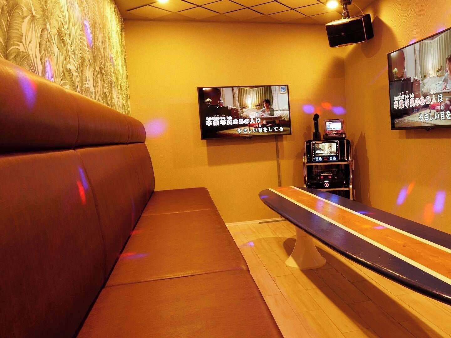 A room with a sofa, a TV mounted on the wall, and a console table with a screen.