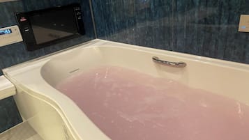 Une baignoire remplie d’eau rose, une horloge numérique et un panneau de commande au mur.