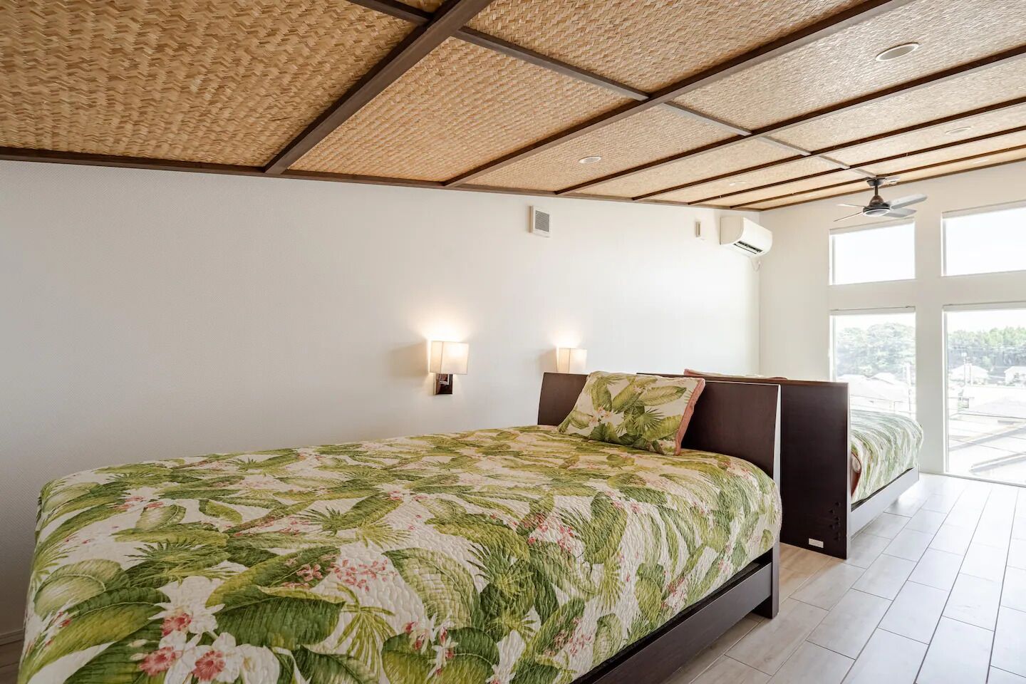 A bedroom with a bed, two wall-mounted lights, a ceiling fan, and large windows.