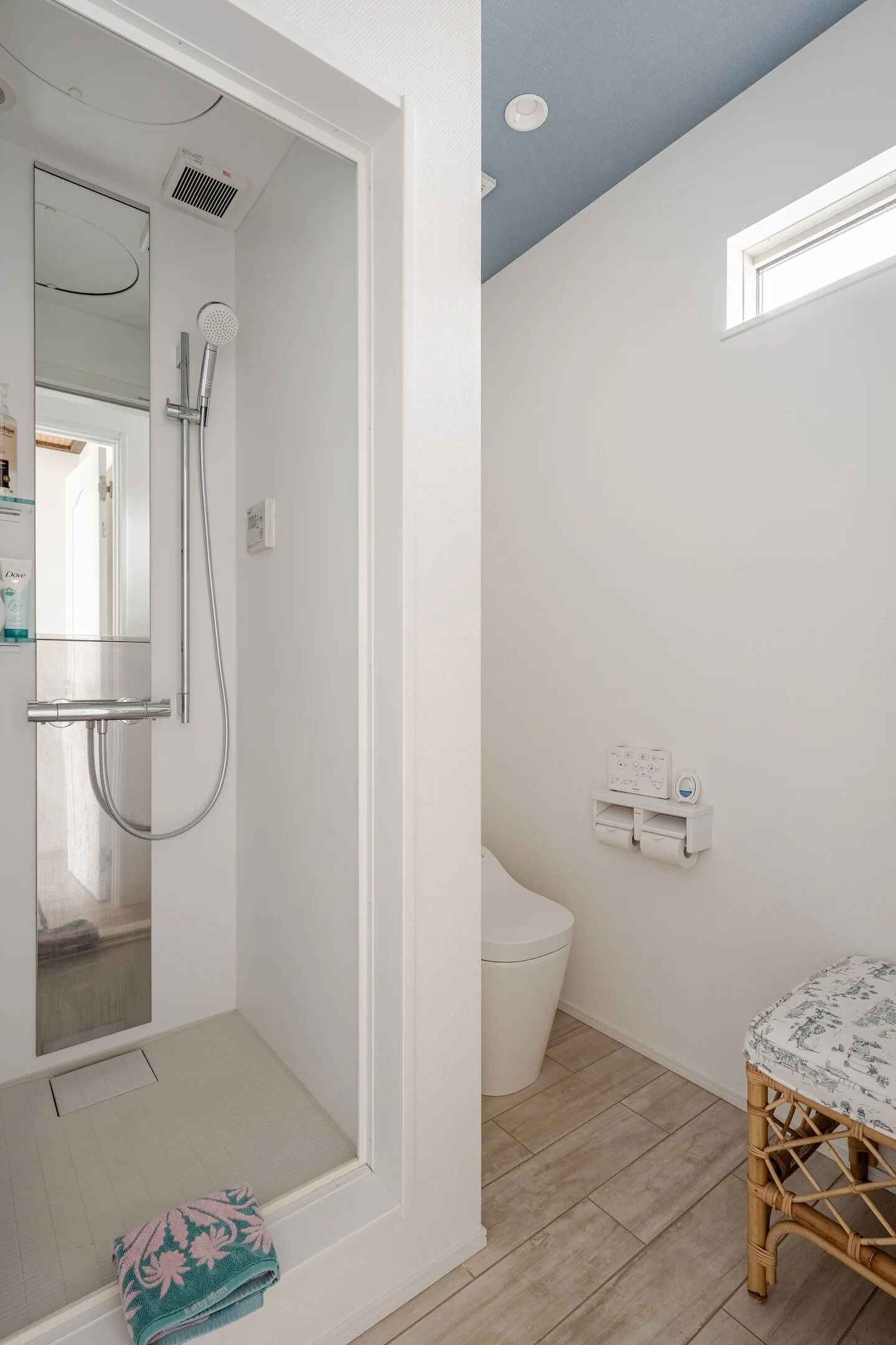 Une salle de bain avec une douche, des toilettes et une petite table recouverte d’une nappe à motifs.