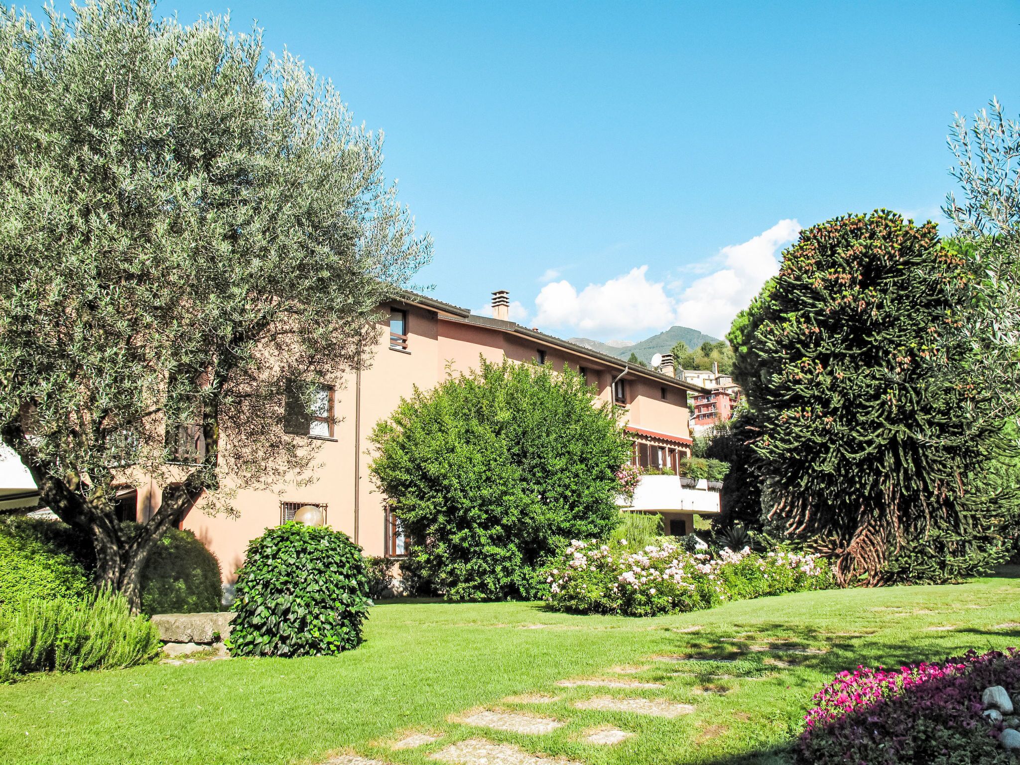 A building with a garden in front, surrounded by trees and shrubs.