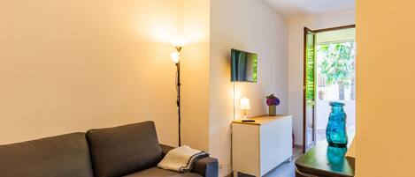 Un salon moderne avec un canapé, une lampe, une petite table sur laquelle est posé un vase, et une vue sur la verdure à l’extérieur.
