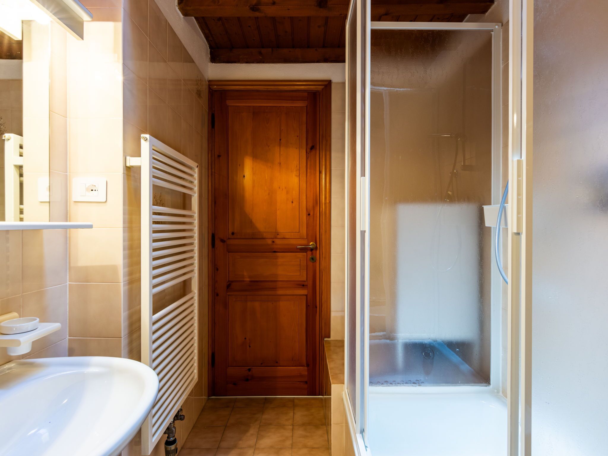 Un bany amb una porta de fusta, una dutxa i un lavabo blanc.