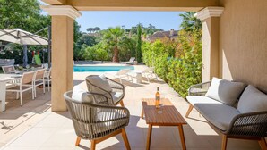 A covered outdoor area with a pool, wicker furniture, and a view of the surrounding greenery. - Villa Julia by Interhome (Les Issambres)