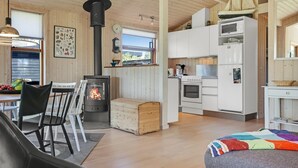 A cozy cabin interior with a central wood-burning stove, white cabinetry, and a dining area with chairs and a table. - "Gligorij" - 450m from the sea by Interhome (Sæby)