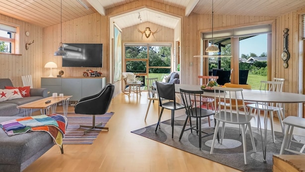 A spacious living area with a wooden interior, a television, a dining table with chairs, and a large window offering a view of the outdoors. - "Gligorij" - 450m from the sea by Interhome (Sæby)