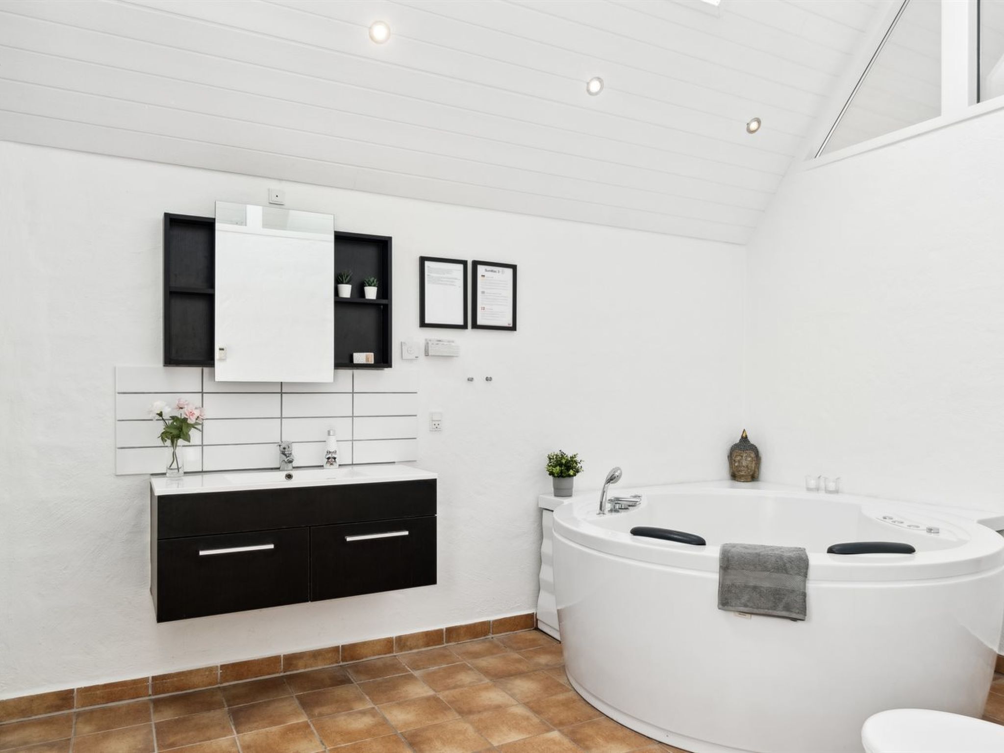 A modern bathroom with a black vanity, white tiles, a large bathtub, and a small potted plant.