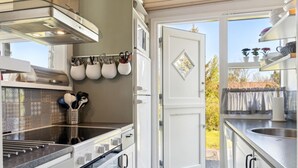 Una cocina moderna con armarios blancos, horno empotrado y campana extractora de acero inoxidable. Hay ollas y sartenes colgando sobre la estufa, y una ventana con vistas al exterior.