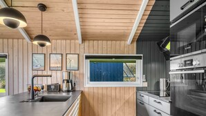 Een moderne keuken met houten lambrisering, een groot eiland met een spoelbak, een Bosch oven en een raam met uitzicht.