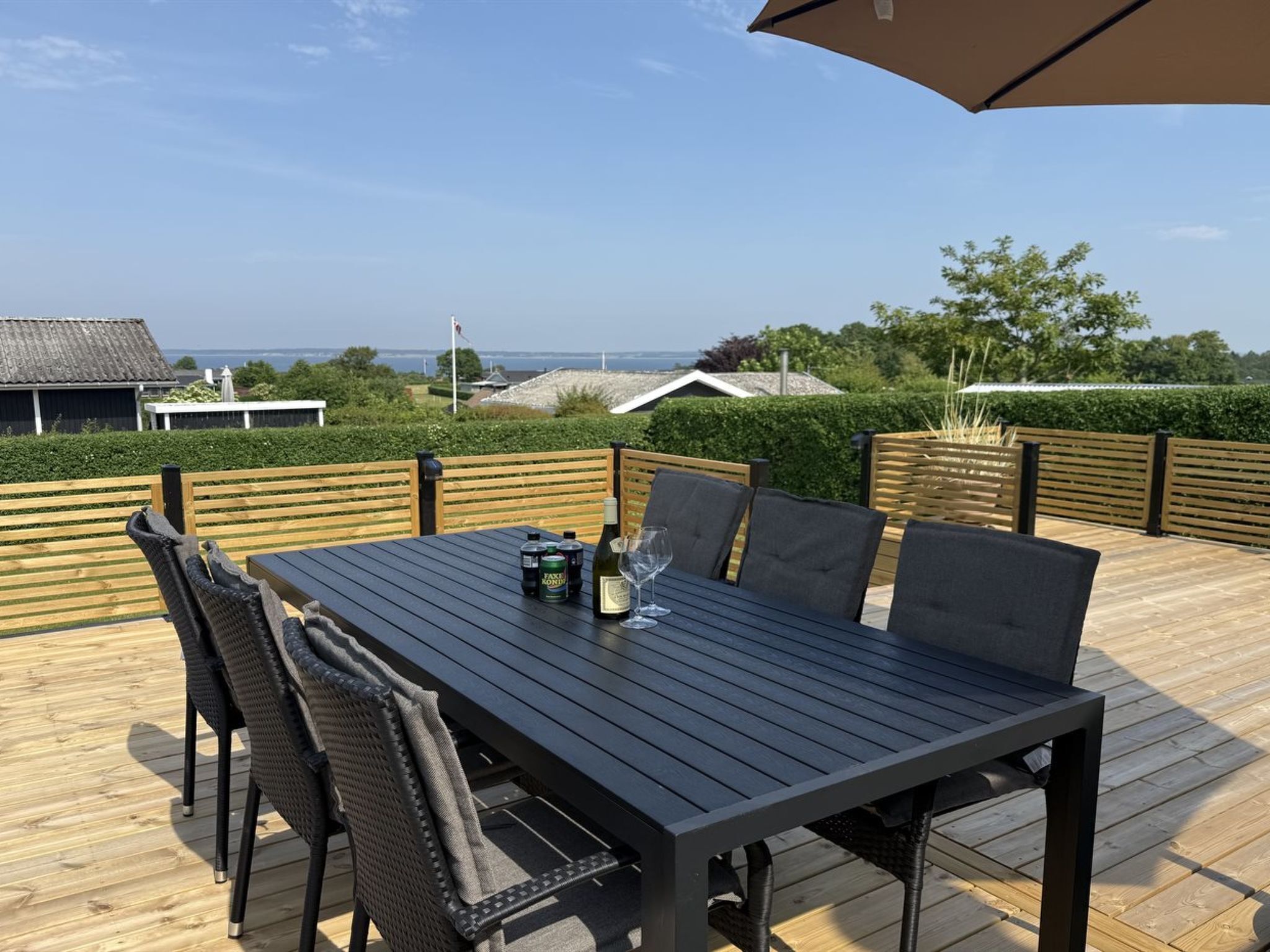 Een houten terras met een tafel, stoelen, een fles wijn en een glas.