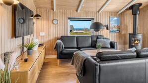 Een gezellig chaletinterieur met houten inrichting, een bank, een tafel, een open haard en uitzicht door het raam.