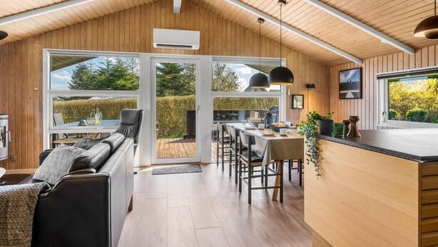 Een modern interieur met een houten plafond, een eethoek, een keuken en een zithoek met uitzicht op het omliggende landschap.