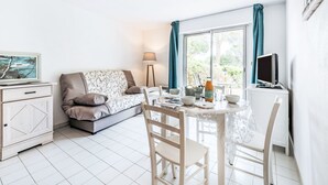 Une pièce moderne et bien éclairée, comprenant un canapé, une table à manger, des chaises, un téléviseur et une fenêtre avec des rideaux.