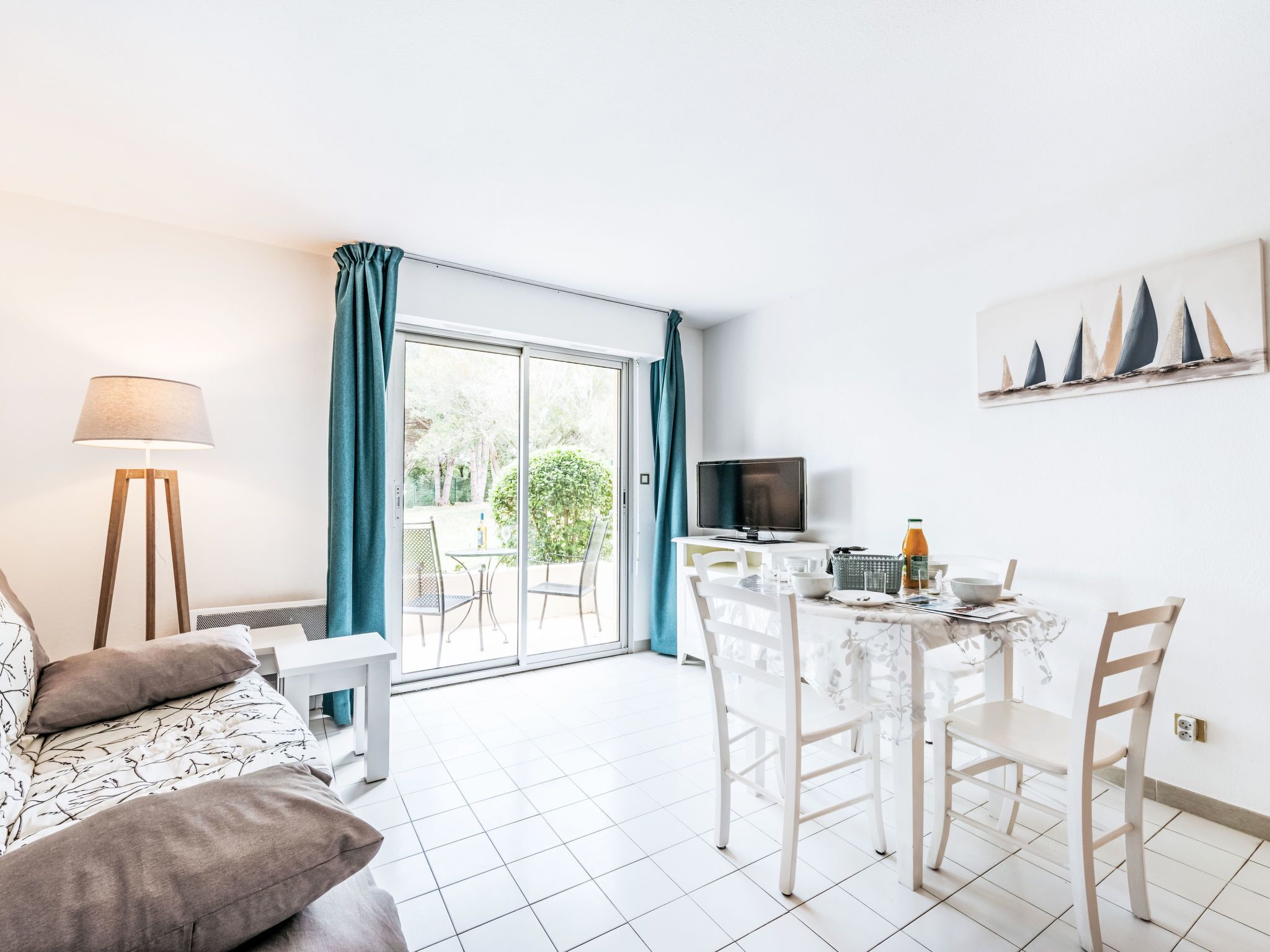 Ein modernes Wohnzimmer mit einer Couch, einem Esstisch mit Stühlen, einem Fernseher und einem Balkon mit Vorhängen.