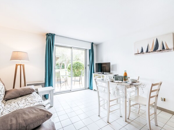 Ein modernes Wohnzimmer mit einer Couch, einem Esstisch mit Stühlen, einem Fernseher und einem Balkon mit Vorhängen.