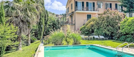 Una piscina rodeada de abundante vegetación y un edificio con balcones.