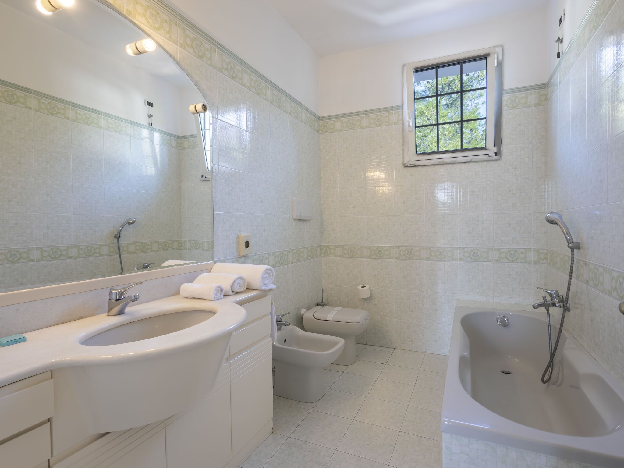 Une salle de bain avec un grand miroir, un lavabo, un bidet et une baignoire.