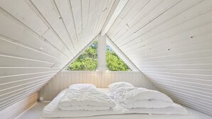 Dormitorio en áticos triangulares con cama, almohadas y vistas a árboles a través de un tragaluz.