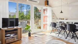 Una sala de estar moderna con un televisor de pantalla plana, una zona de comedor con sillas y un amplio ventanal corredero que da a un patio exterior.