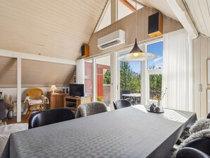 Un comedor con mesa, sillas, televisor y ventana con vista a follaje.