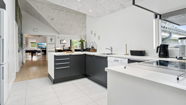 A modern kitchen with a central island, a dishwasher, and a coffee machine. There is a skylight above the island and a view of the outside through a window.