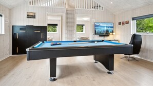 A pool table in a room with wooden walls, a TV mounted on the wall, and a window with a view of trees.