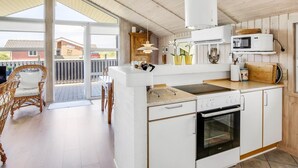 Una cucina moderna con mobili bianchi, forno integrato e microonde. C'è un'area pranzo con sedie in vimini e un tavolo.