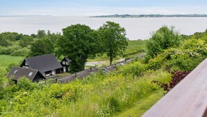 Een huis aan de kust met uitzicht op zee, omringd door weelderige begroeiing en een houten terras.
