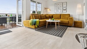 Een moderne woonkamer met een mosterdgele bank, een glazen eettafel en een balkon met uitzicht.