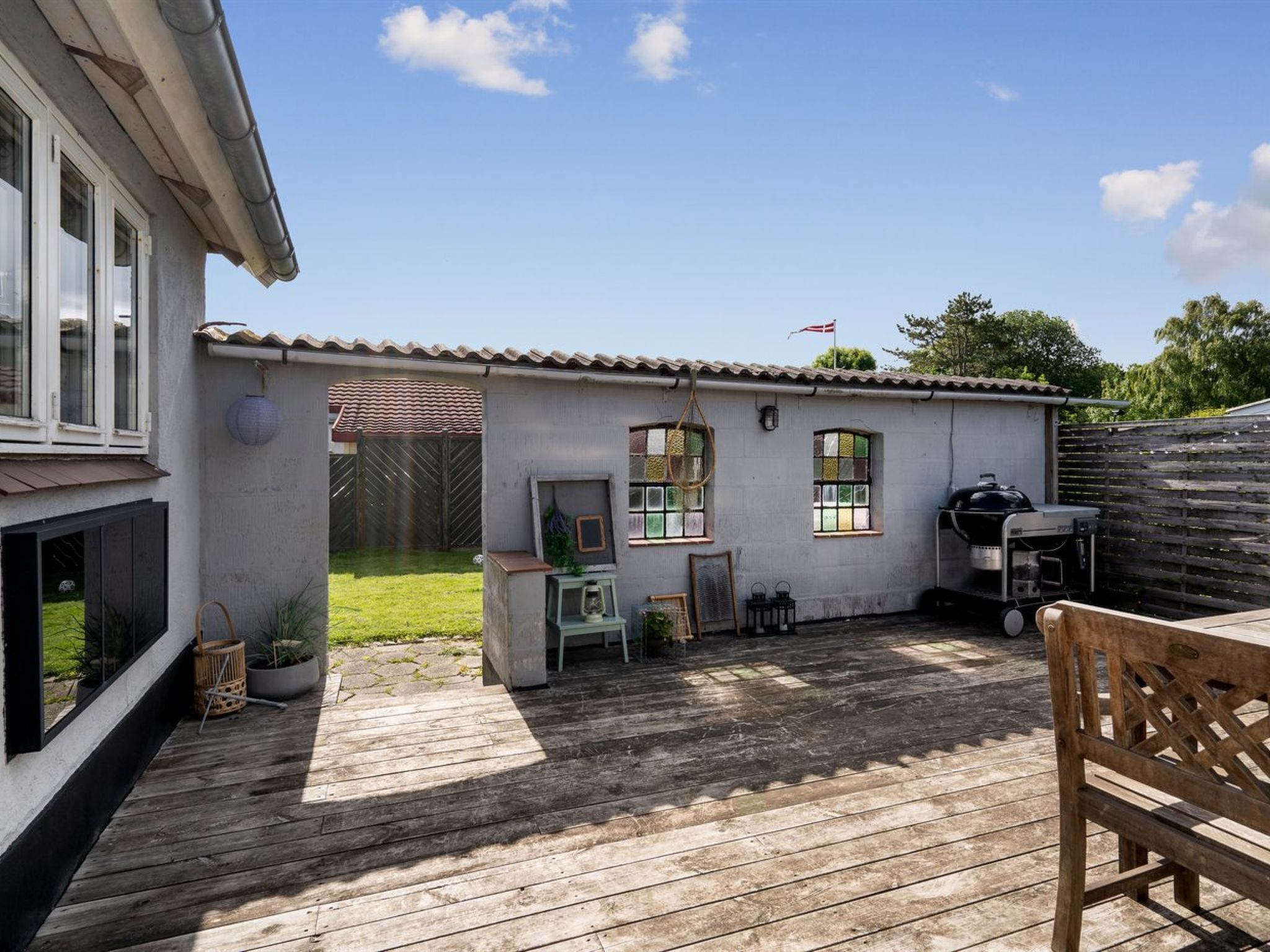 Een houten terras met een barbecue, een tafeltje en een stoel.